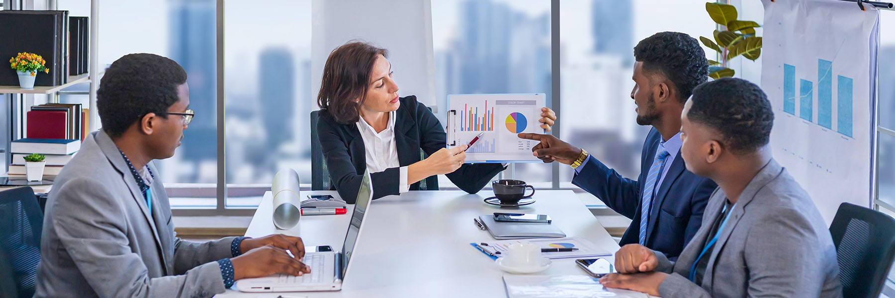 Four people sitting around conference table looking at a chart being held by the one at the end