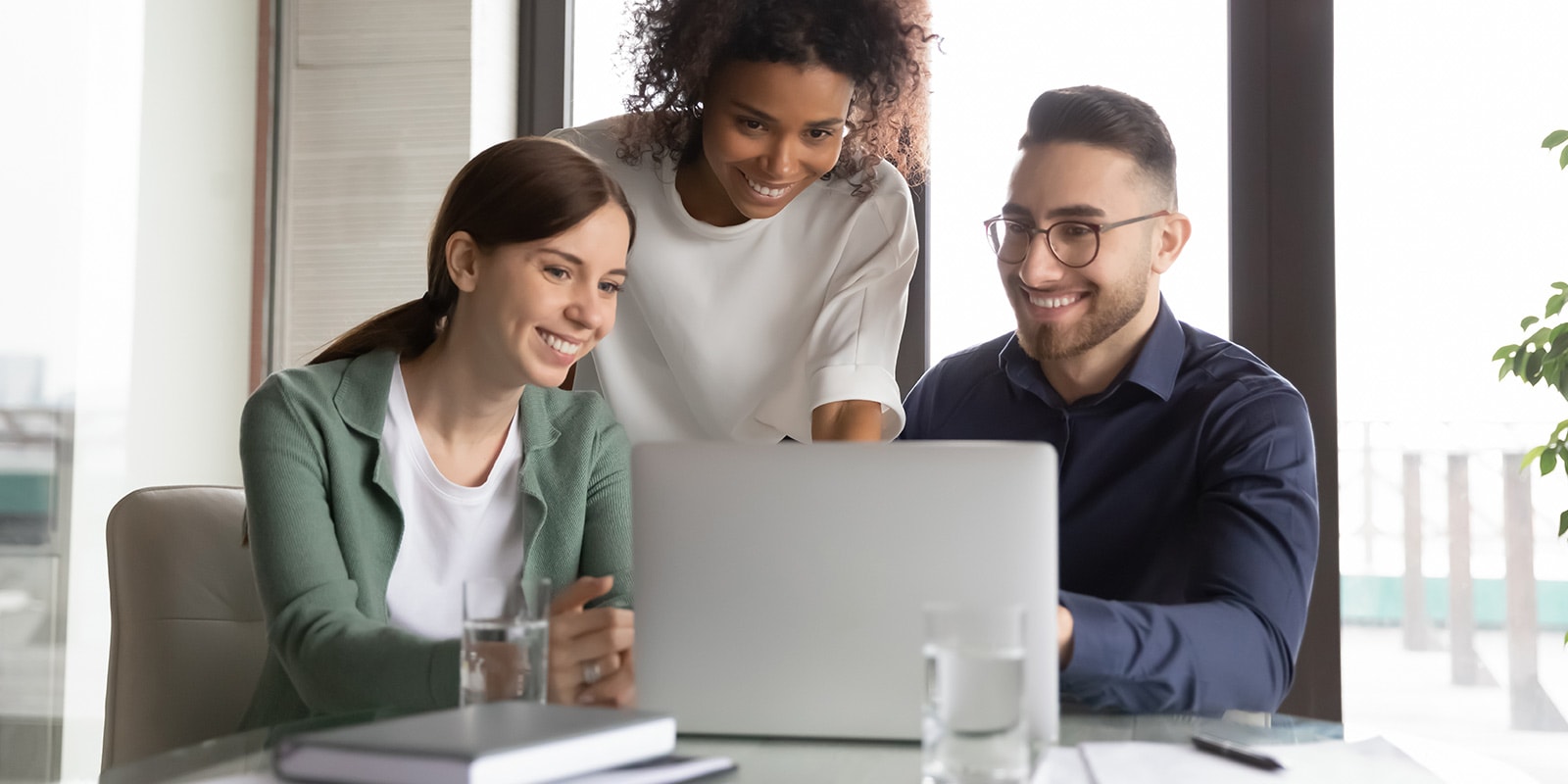 Three happy diverse colleagues working on project together, using laptop