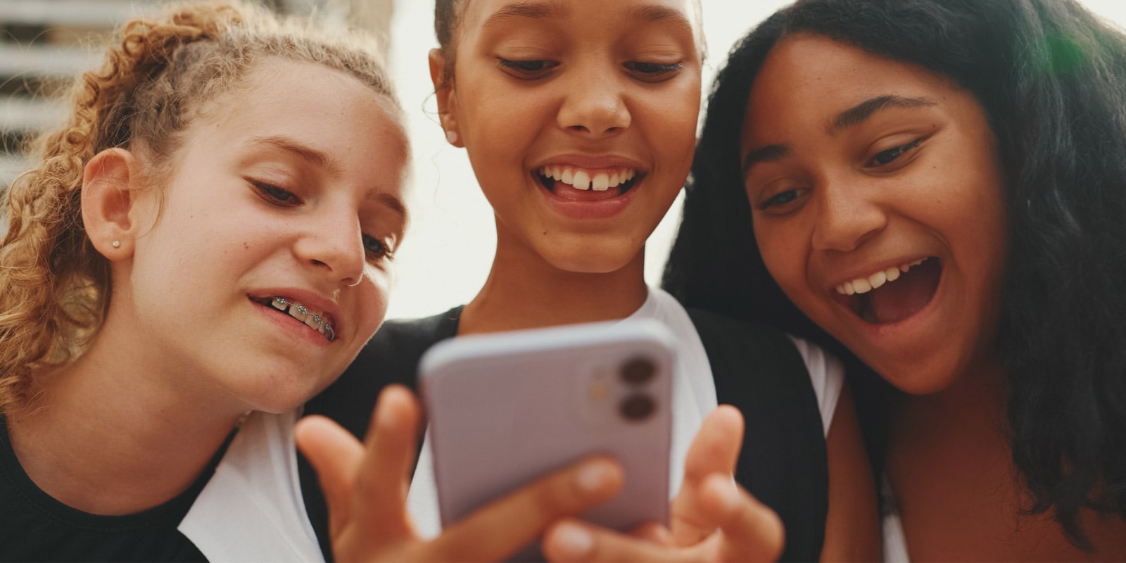 A diverse group of three girls smiling while looking at a smartphone in a close setting.
