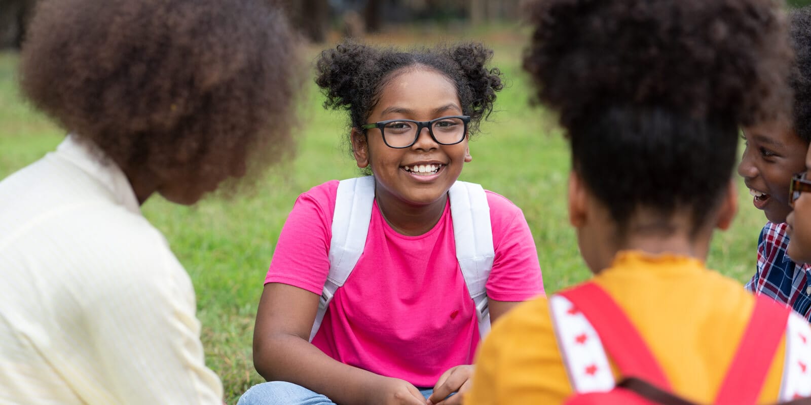 Four students sitting in a circle, one facing camera with big smile.