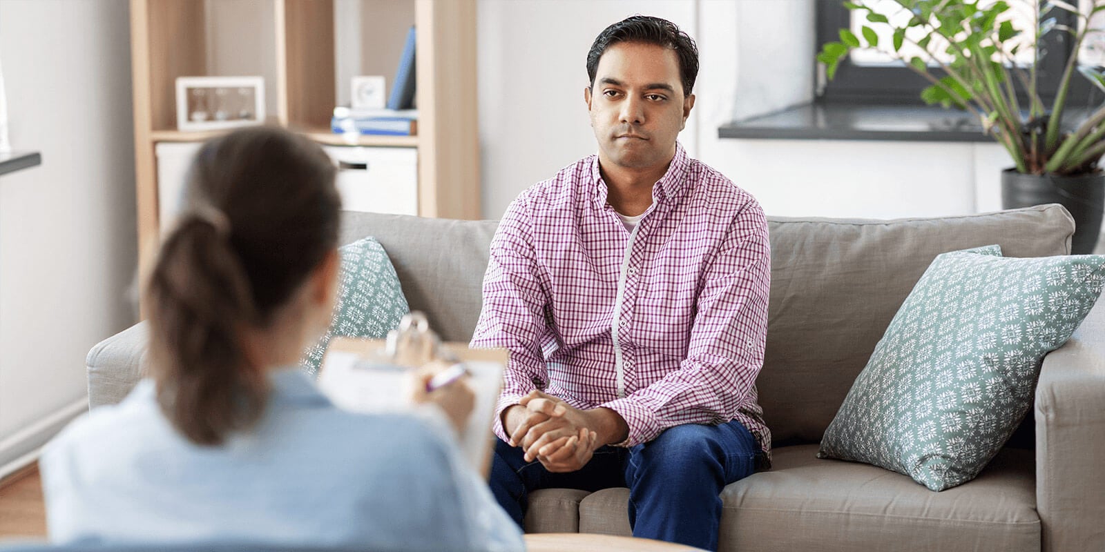 Man sitting on a couch speaking with a woman who is taking notes on a clipboard