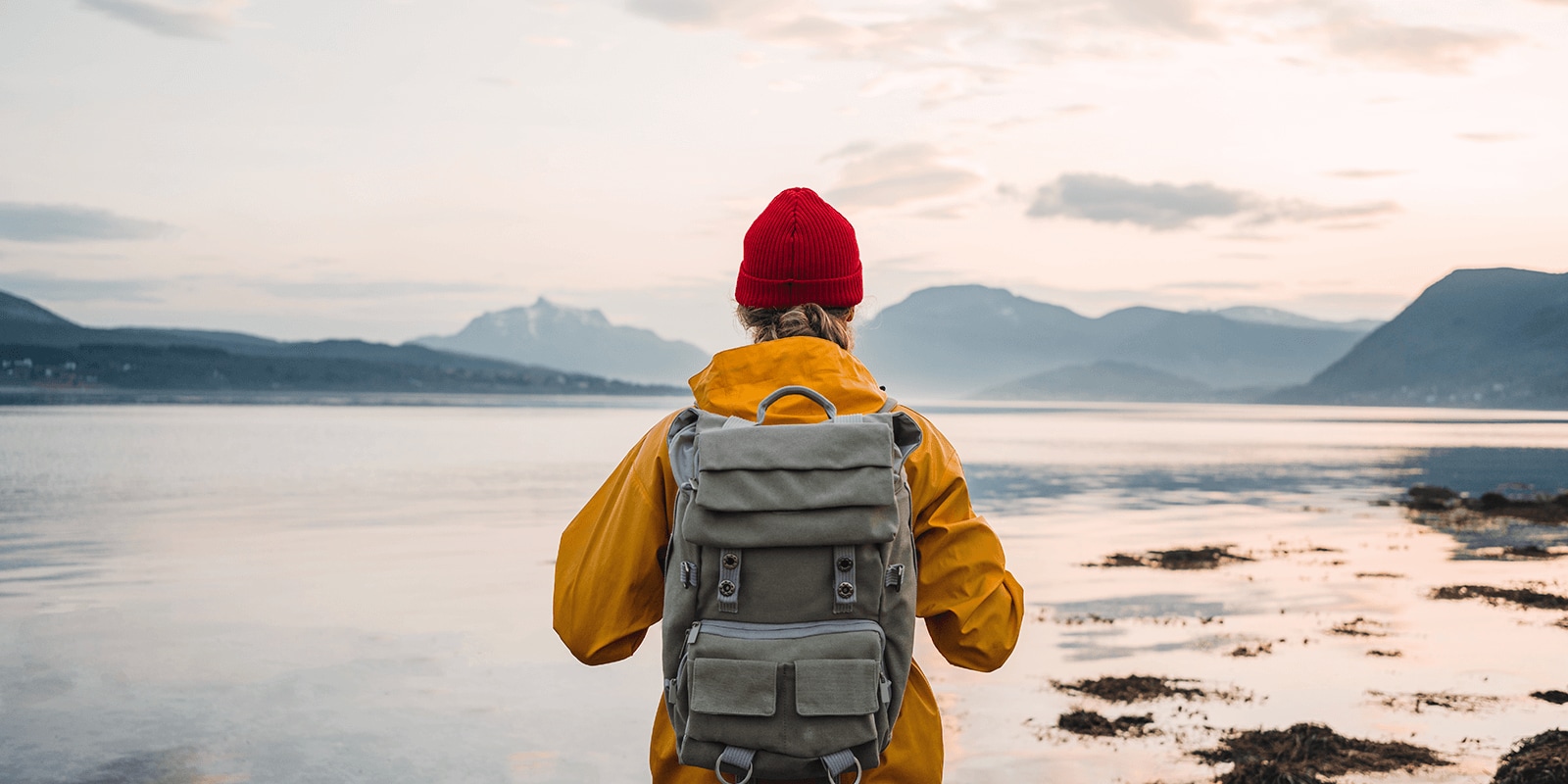 Hiker with backpack facing water and mountains