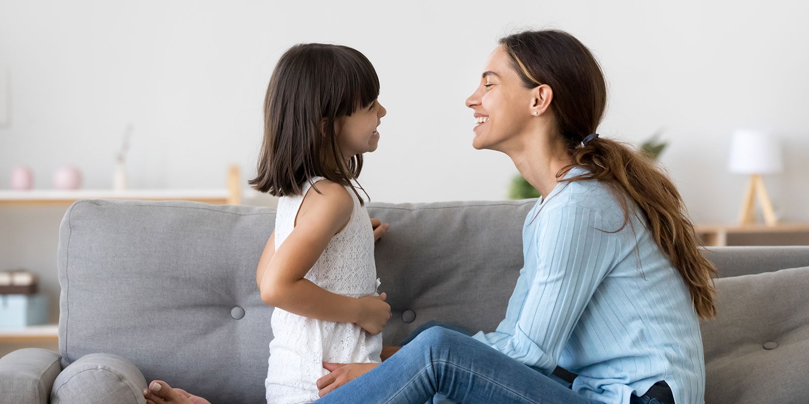 Mother and daughter sitting on the couch smiling at one another.