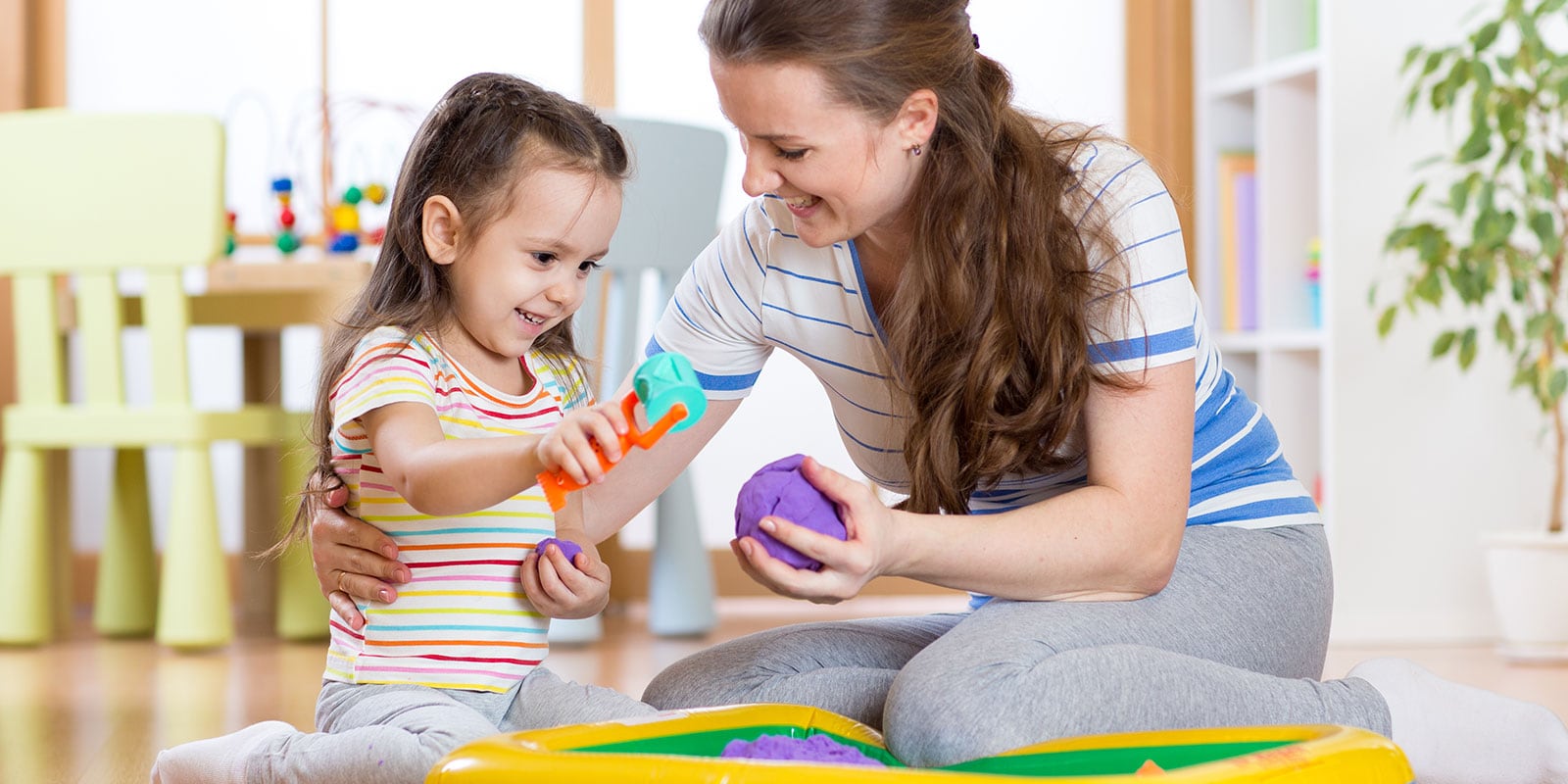 Mother and young daughter playing with block on the floor. 