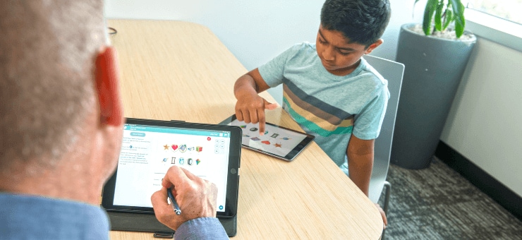 Two individuals at a table; one adult and a young child, each using a tablet, in a bright office setting.